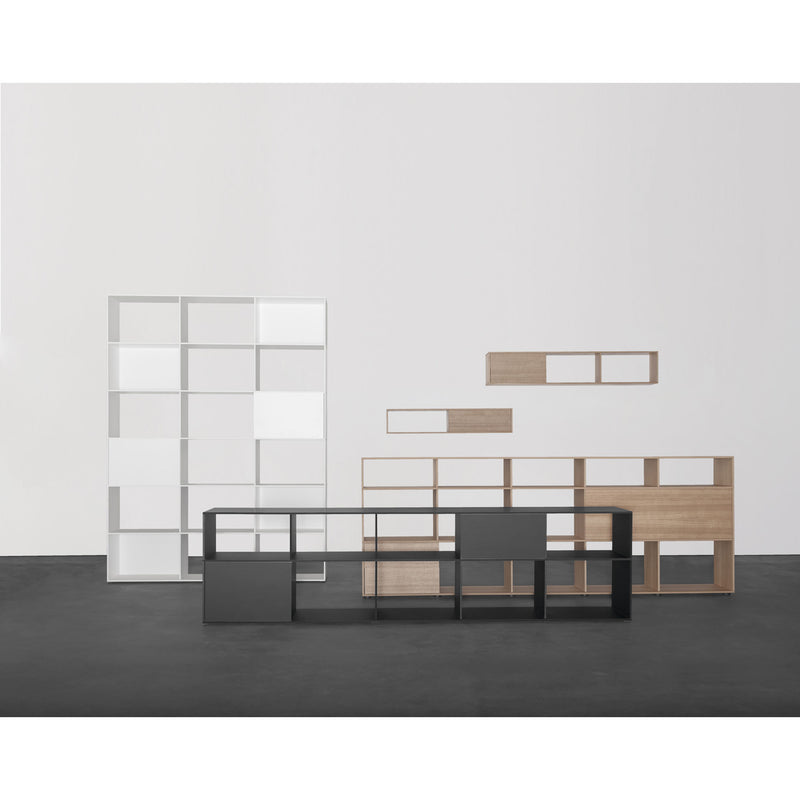 In a minimalist interior, the Tektur sideboard by Sanktjohanser showcases a customizable shelving system. Modular shelves in oak veneer, white, and black grace a plain white wall on a dark floor, offering style and flexibility with optional sliding doors.