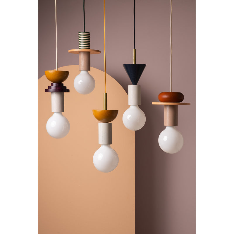 Schneids Junit Omen, with its modular pendant lamps in yellow, orange, black, and beige, features exposed bulbs suspended from a two-toned wall. Each lamp has a uniquely shaped colorful fixture casting ambient light to form an artistic display.