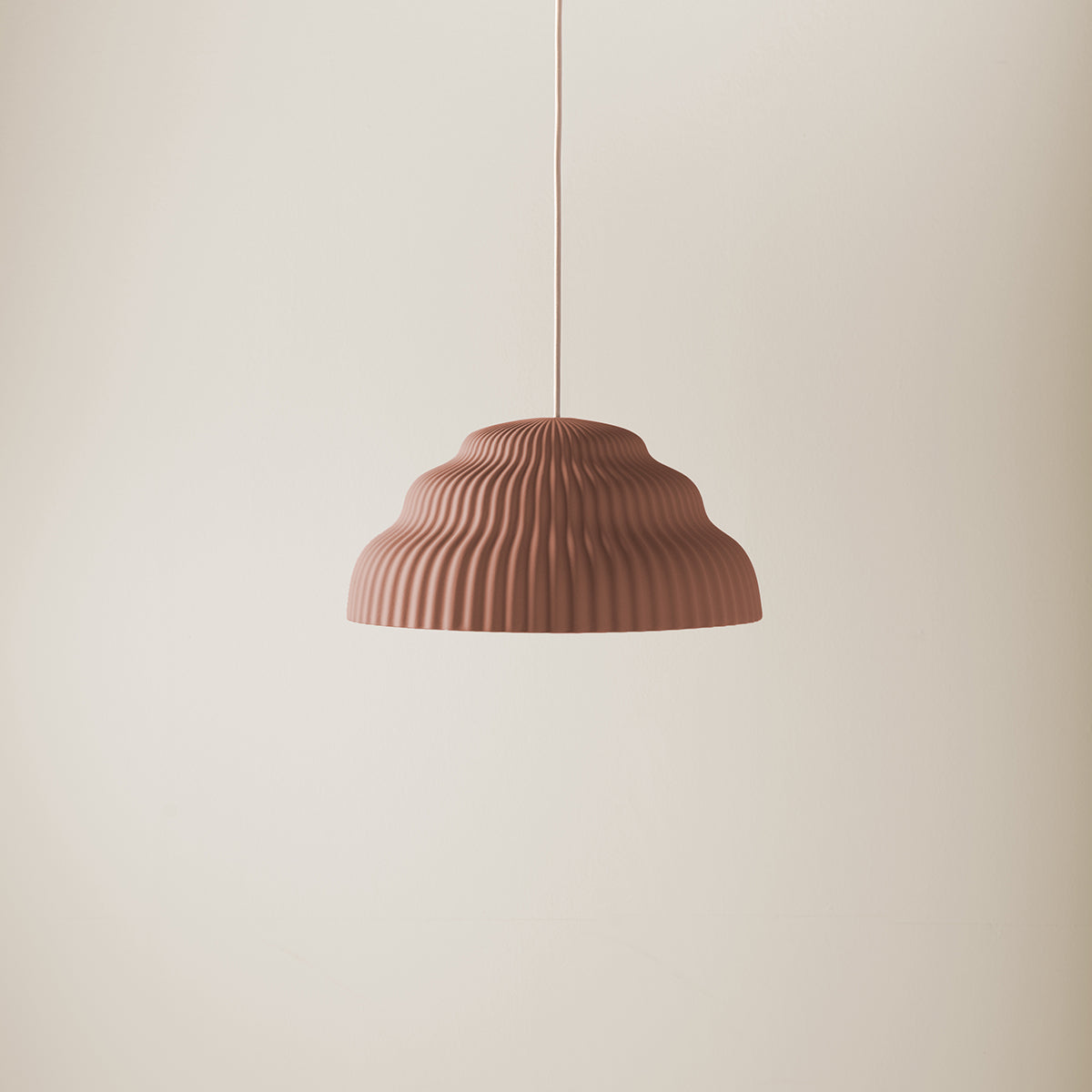 A Kaskad Rust lamp by Schneid, featuring a brown ribbed dome shape, hangs from a thin cord against a plain beige backdrop.