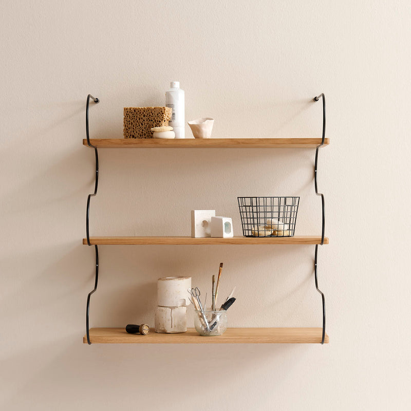 The Onda by Schneid offers modular oak wall shelves with elegant curves and black metal brackets, perfect for holding sponges, bottles, small bowls, metal wire baskets, rolls, and jars with brushes. These shelves beautifully complement cream-colored walls.
