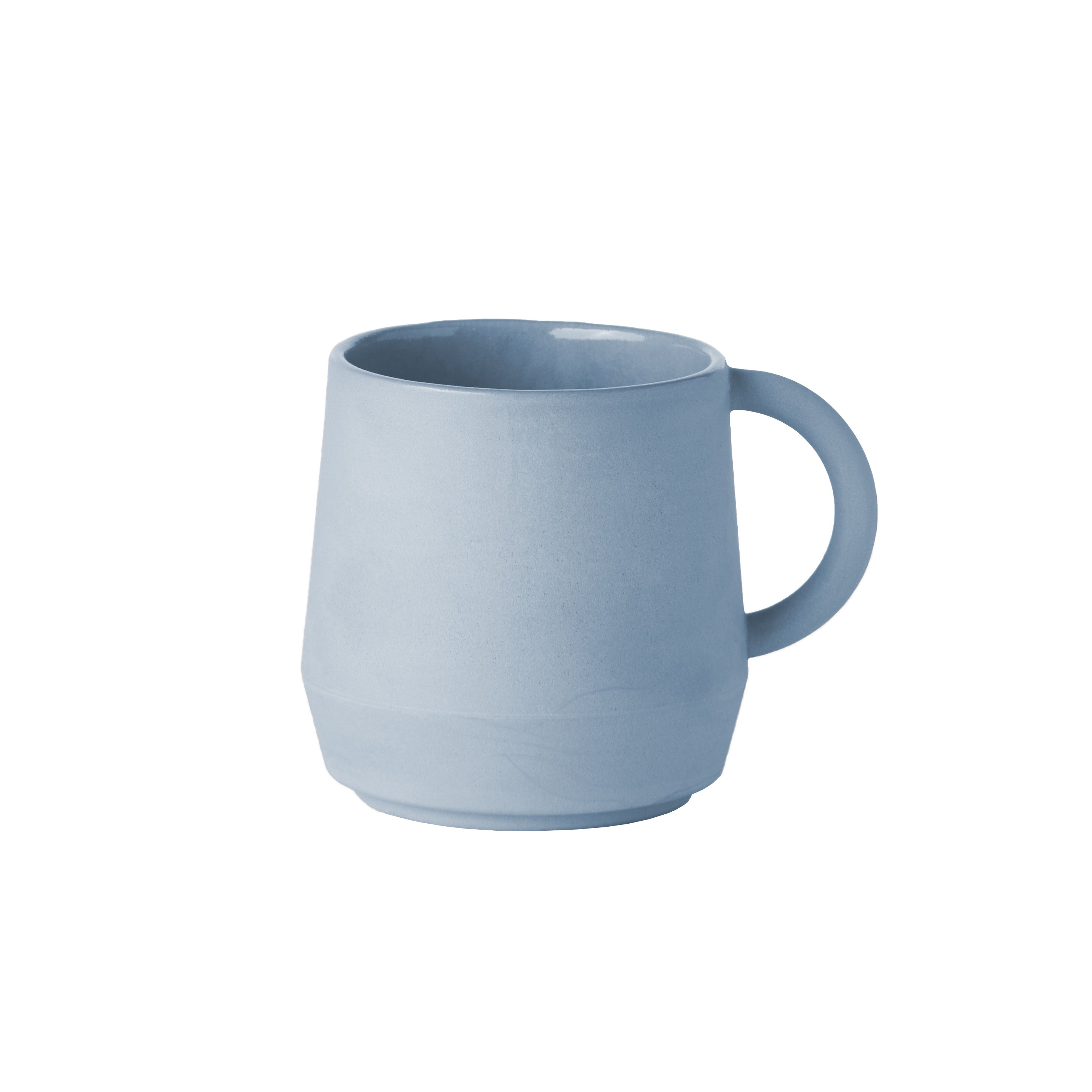 The Unison Cup by Schneid is a handmade, minimalist ceramic mug from Germany with a smooth, matte finish, light blue color, sturdy handle, and slightly tapered shape. Perfect for stacking with other ceramic tableware on white backgrounds.