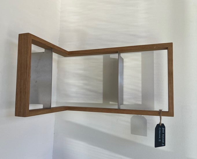 The b corner - Sale by Das kleine b is mounted on a light-colored wall, featuring a unique angled wooden design with embedded stainless steel angles. It includes a metal bar for hanging towels and blends style with function, complete with a small tag on the bottom right corner.