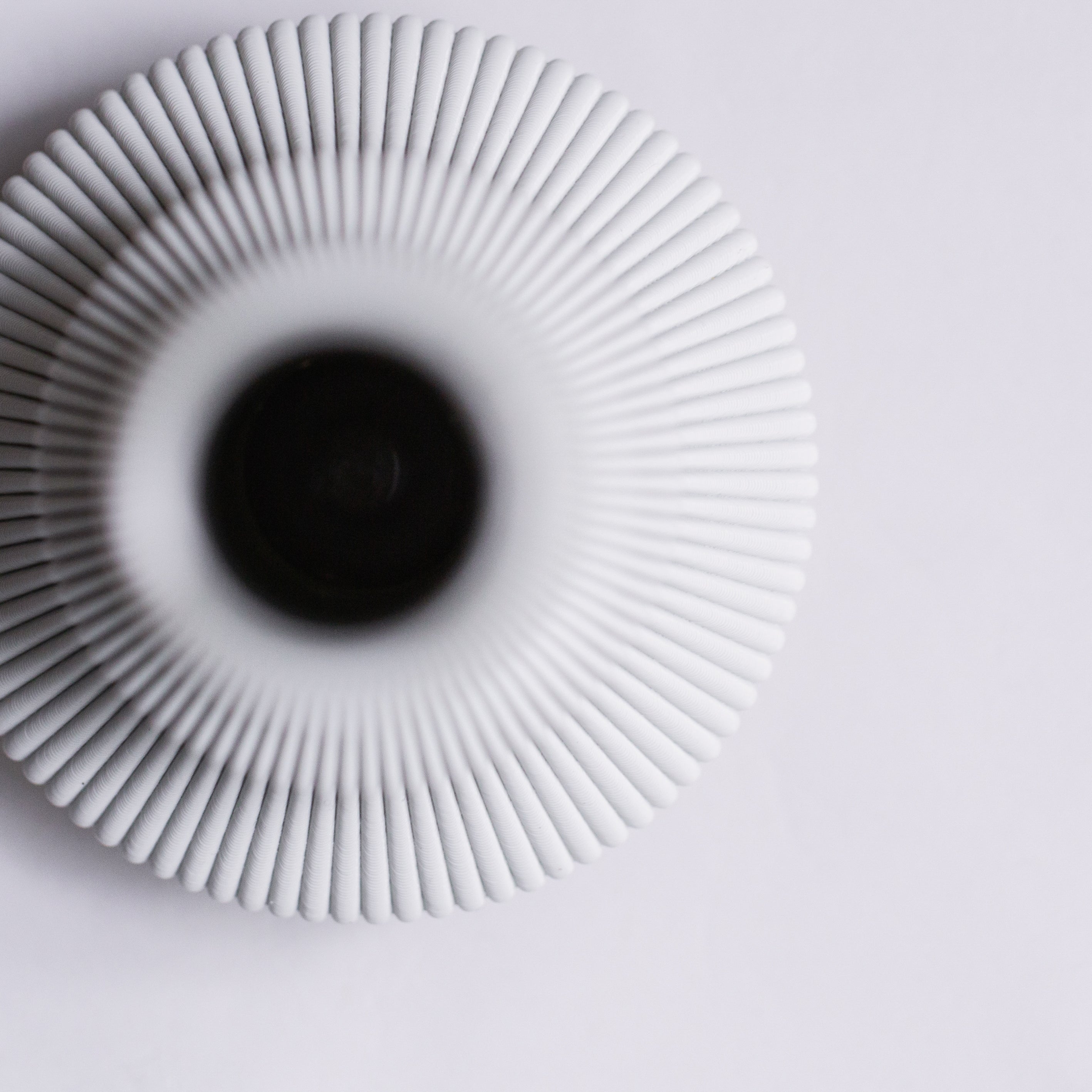The Zayl 114g Vase by Sheyn is a white, ribbed, round ceramic piece with a central opening viewed from above. Set against a white backdrop, it highlights its textured surface and symmetrical elegance.