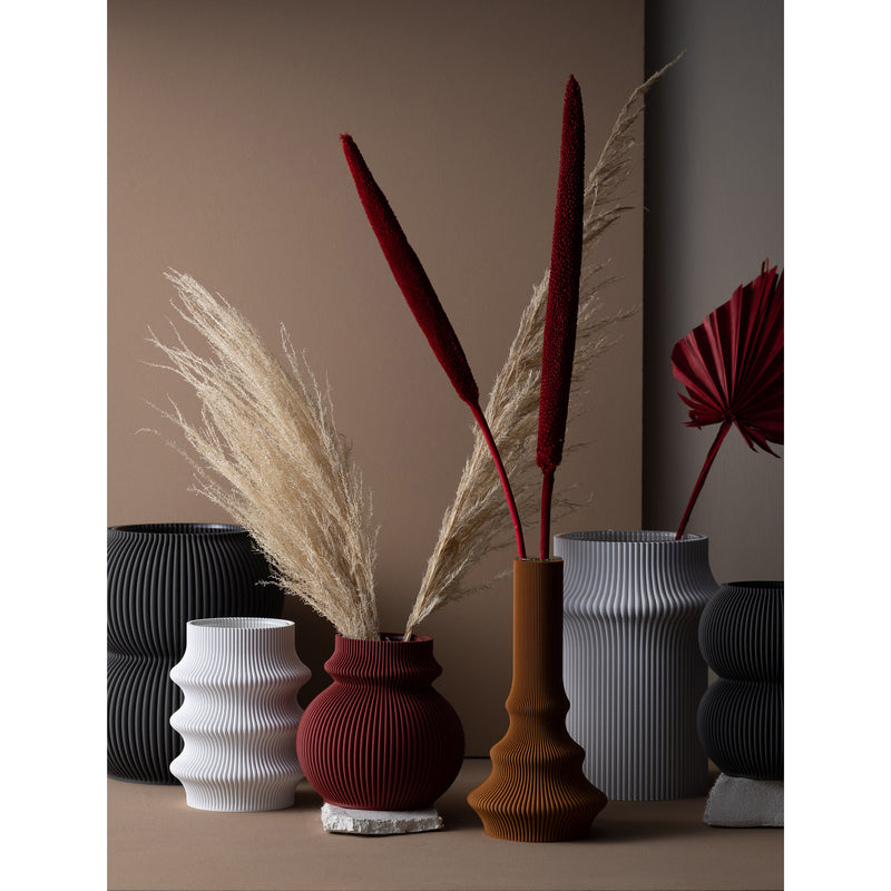 The Sheyn Zayl 129g Vase collection includes ribbed vases in various shapes and earthy tones, crafted using digital design and 3D printing. Ideal for holding dried pampas grass or decorative red stems, they create a modern, minimalist display with an eco-friendly touch.