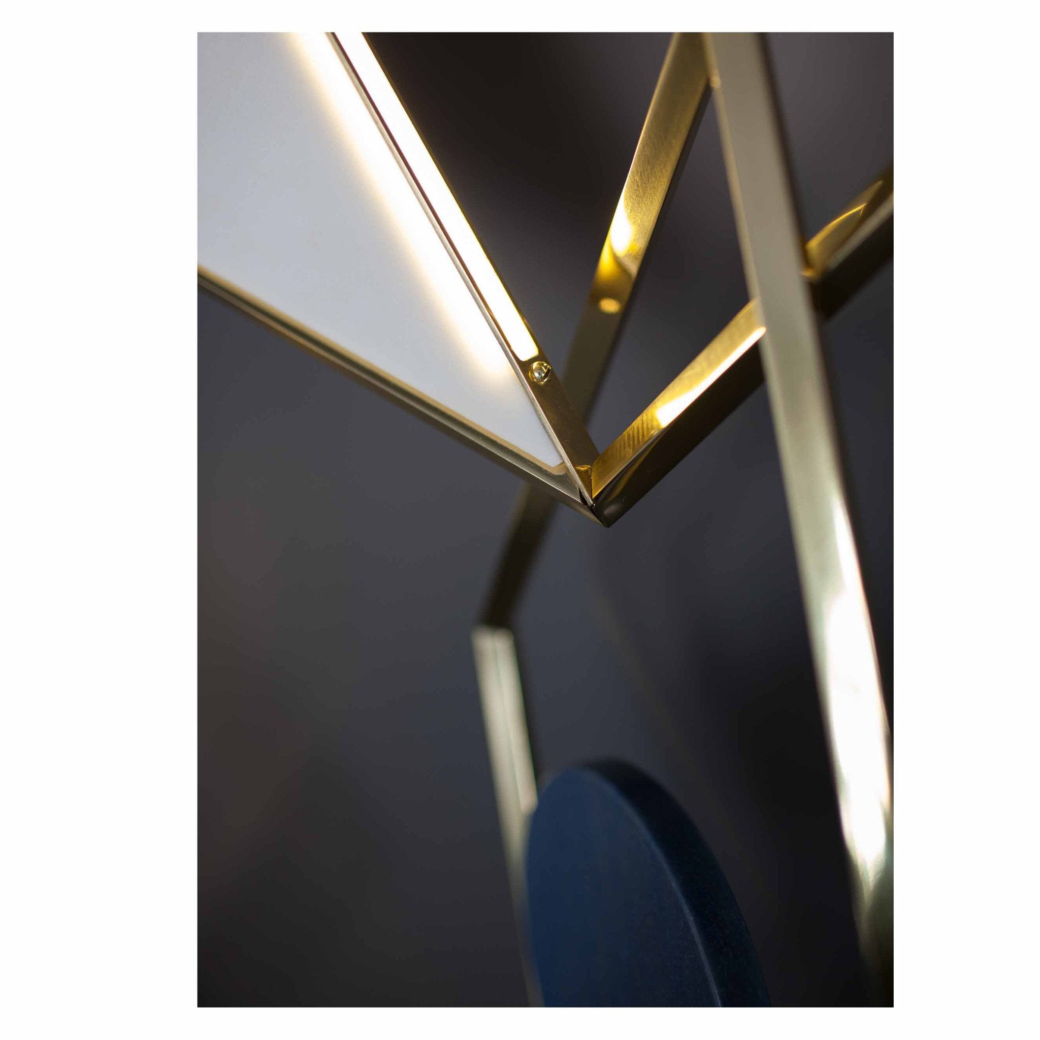 A close-up shows the Tangle Light by Coordination Berlin, featuring a sculptural, angular design with gold metal frames and a white translucent shade. Resembling modern jewelry, it is elegantly set against a dark background.