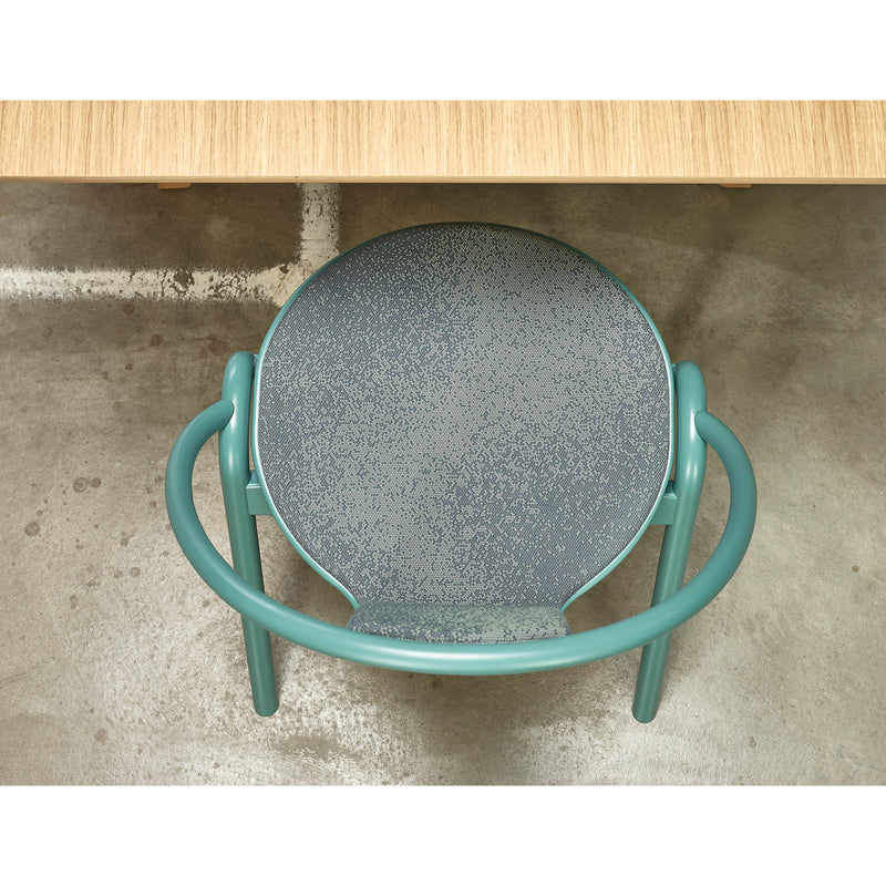 Aerial view of a Chair Again Upholstered by TON in teal metal, featuring a round speckled gray seat. Its placed under a light wooden table on a concrete floor with white markings, resembling stackable dining chairs.