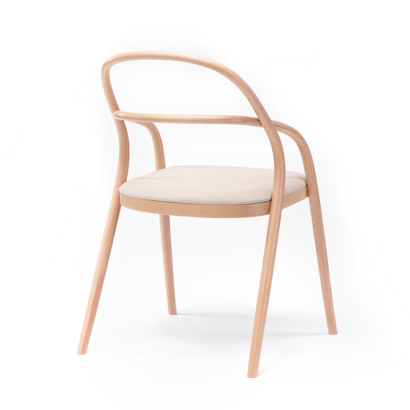 The Chair 002 - Upholstered by TON boasts a minimalist design, resembling the No. 14 redesign. It features a curved backrest, a light beige cushion, and four slender legs, elegantly crafted against a white background.