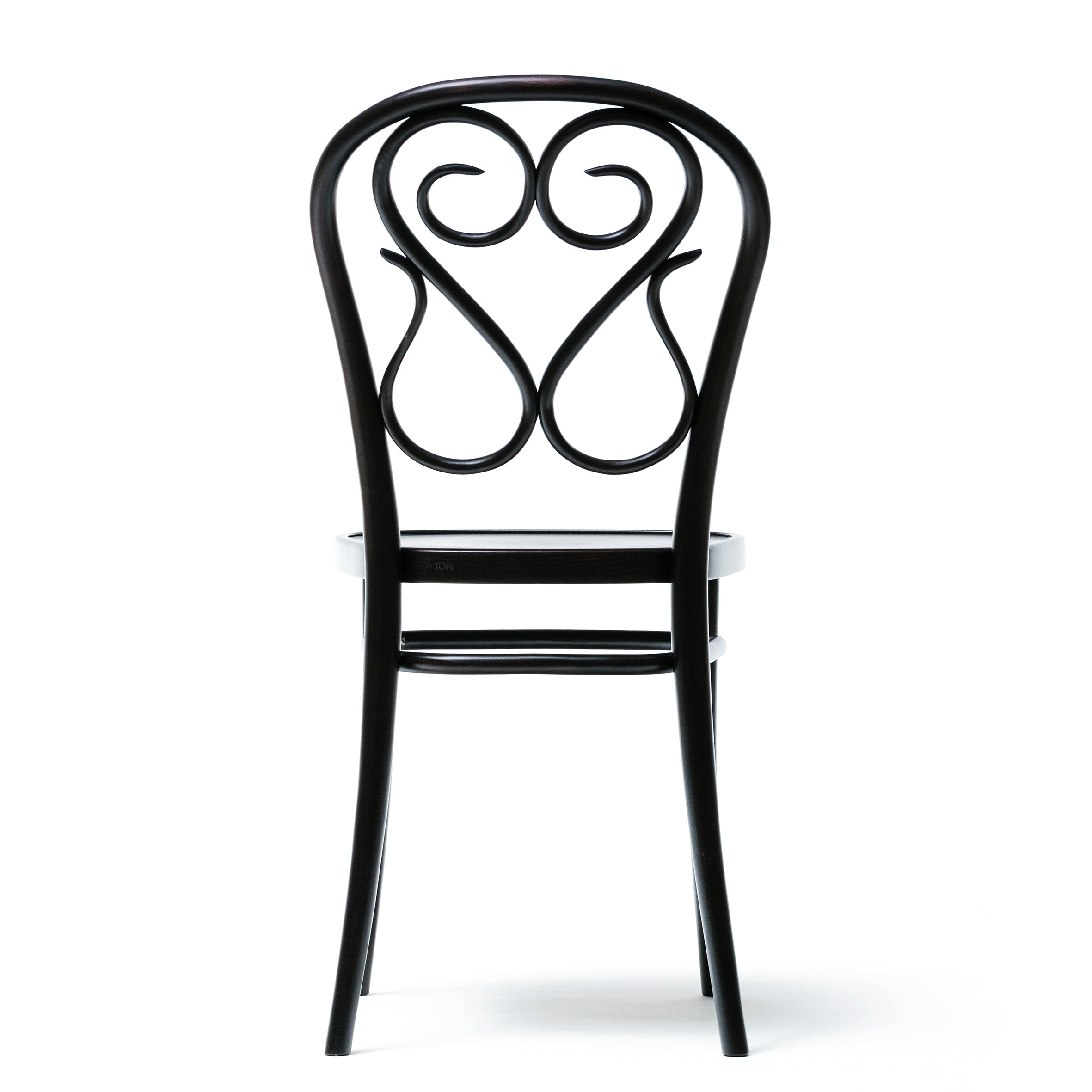 The Chair 04 by TON is a black, ornate dining chair with a decorative swirling backrest and slender legs. Its intricate bent details display elegant curves and loops, while the plain white floor and background accentuate its artistic features as seen from the rear.