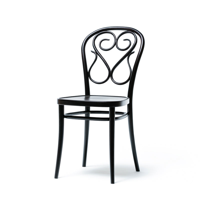 Chair 04 by TON is a black wooden dining chair featuring an ornate, swirling design on the backrest with a rounded top and slender legs. The seat is smooth and flat, showcasing meticulous manual work and intricate bent details.