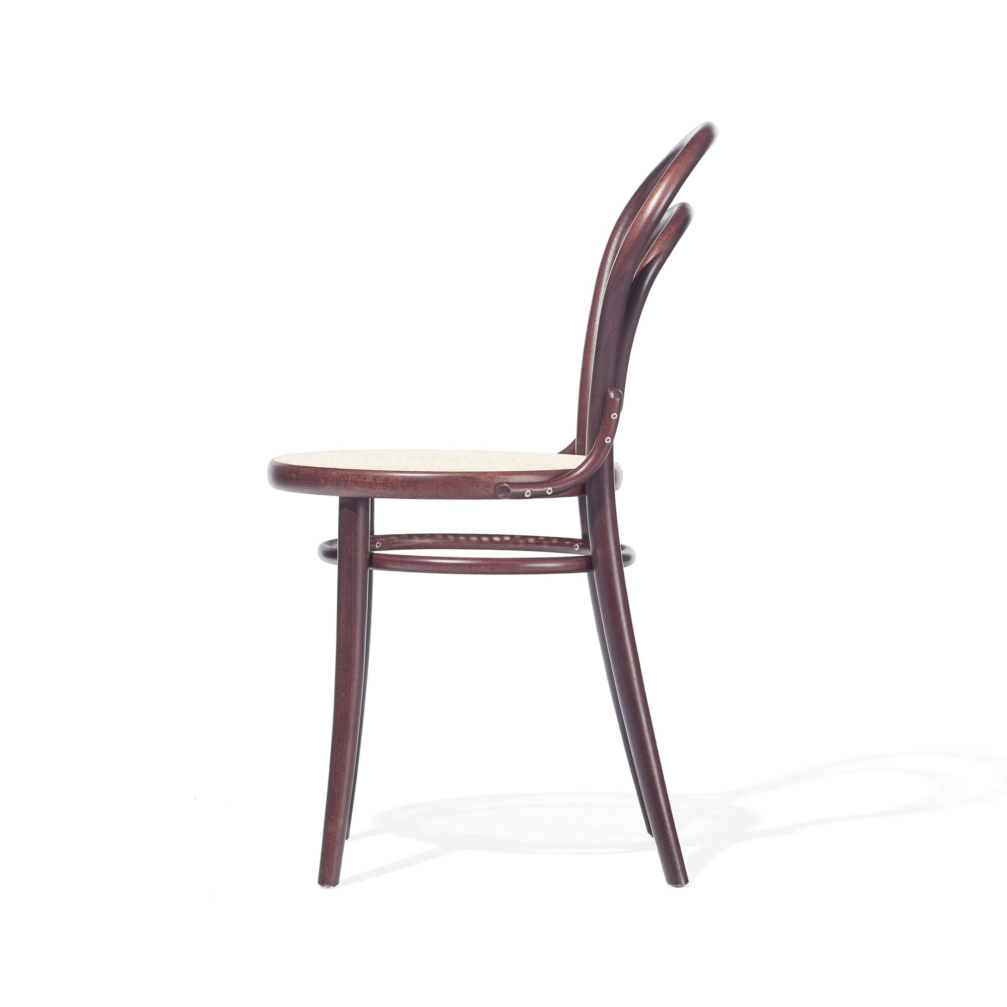 The Chair 14 - Cane by TON features a side view of its classic wooden design with a rounded backrest and cane seat, casting shadows on a white background. Its simple elegance is highlighted by a smooth, dark finish.