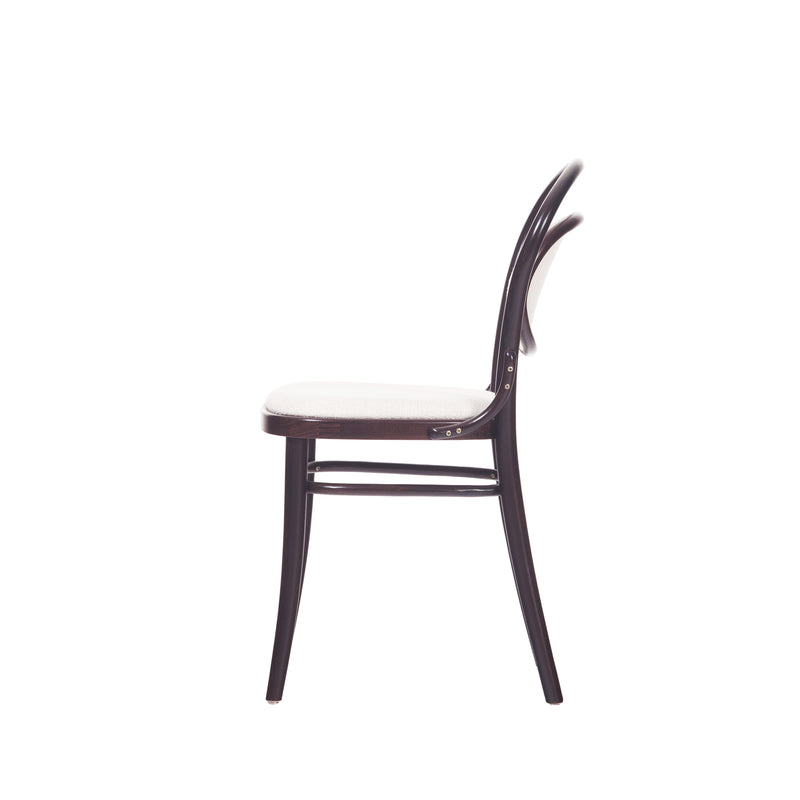 Get a side view of the TON Chair 20 - Upholstered, featuring a curved backrest and light upholstered seat. This wooden chair boasts a sleek, minimalist design with a dark finish and angled legs, providing style and comfort for any dining area.