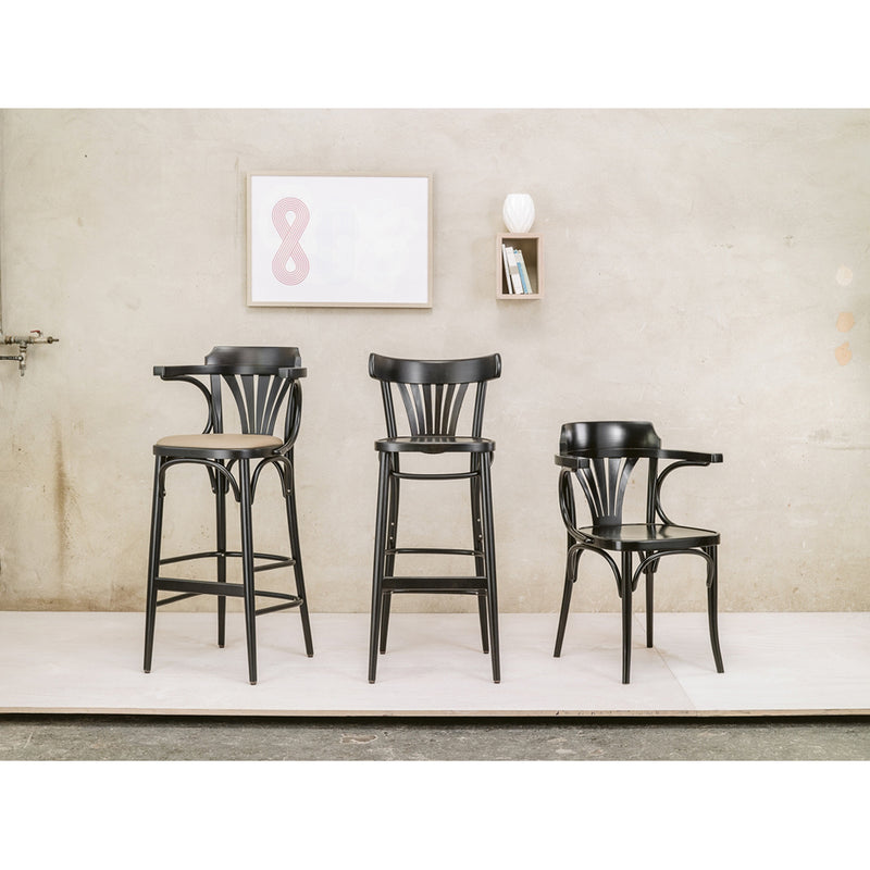Three TON Armchair 25 pieces, black and wooden with fan backrests of varying heights, are placed against a beige wall. Above them is a small shelf with books and a framed print of the number eight. The light floor contrasts strikingly with the dark chairs.
