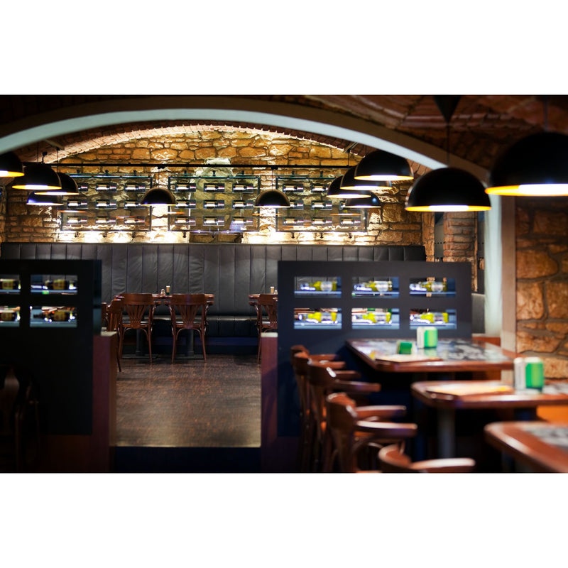 Cozy restaurant with rustic stone walls and wooden furniture, illuminated by warm pendant lights. Tables are neatly arranged, and a lounge area features TONs Armchair 25 with dark seating and upholstered armchairs, enhancing the inviting atmosphere.
