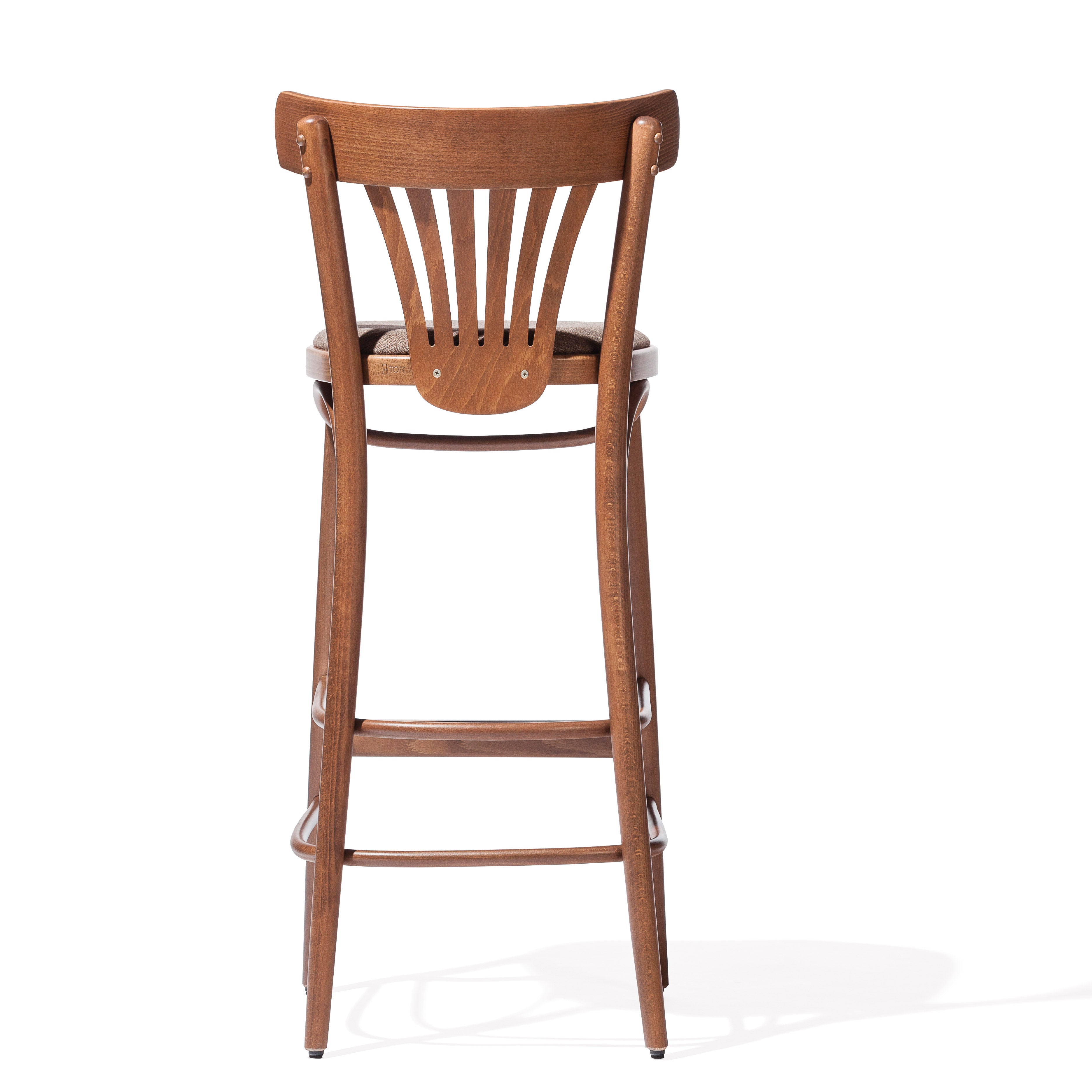 The Barstool 56 by TON is a wooden piece with a curved backrest and vertical slats, finished in warm brown. It features four legs and a footrest. Its shadow on a white background emphasizes its seamless craftsmanship, ensuring comfort without upholstery.