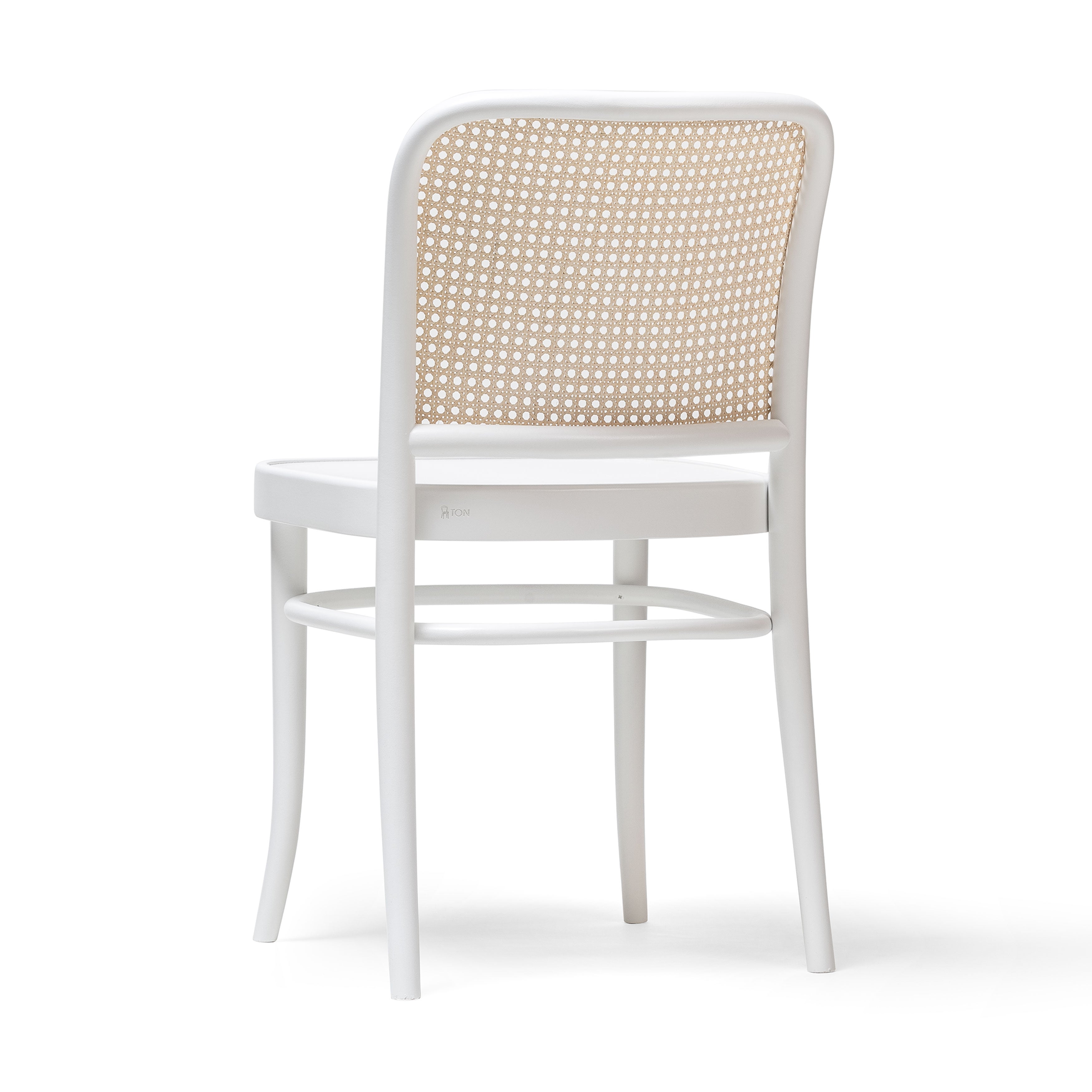 The Chair 811 by TON is a white wooden chair inspired by Josef Hoffmann, featuring an Art Nouveau style with a curved backrest of woven cane. It has four legs and a circular seat, elegantly displayed against a plain background.