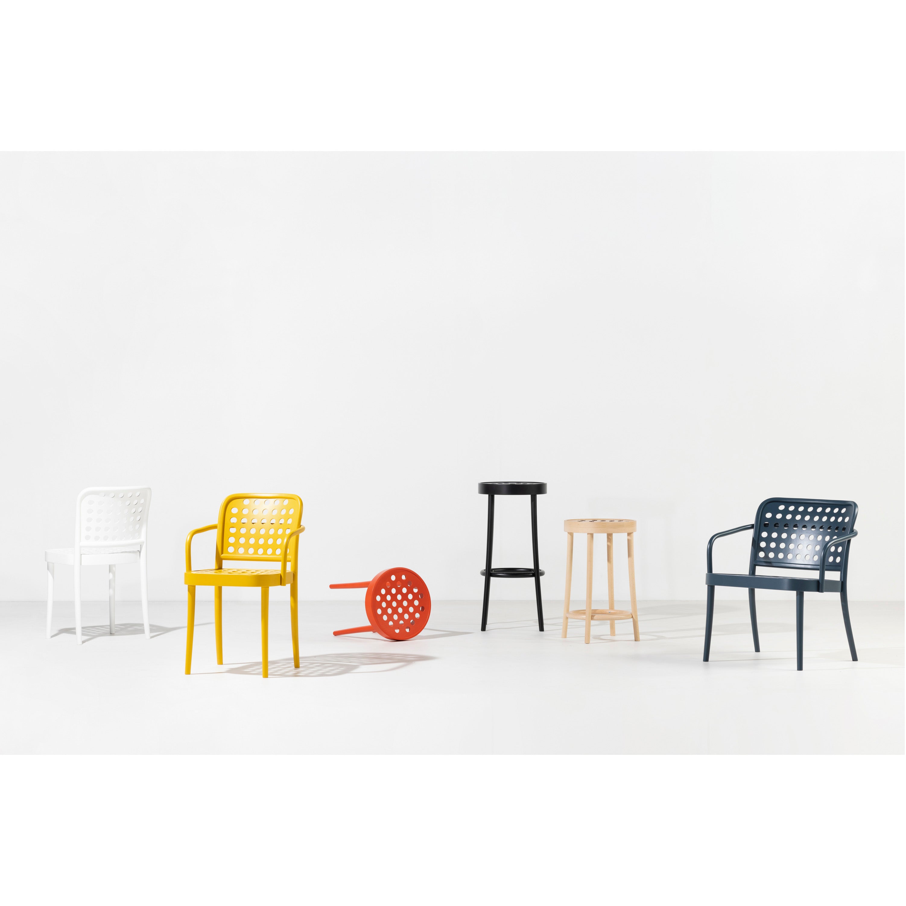 Six TON Chair 822 pieces are arranged against a plain white backdrop, exuding Scandinavian minimalism. They come in white, yellow, red (lying on its side), black, natural wood, and blue, featuring solid and perforated designs that highlight the beauty of manual wood-bending technology.