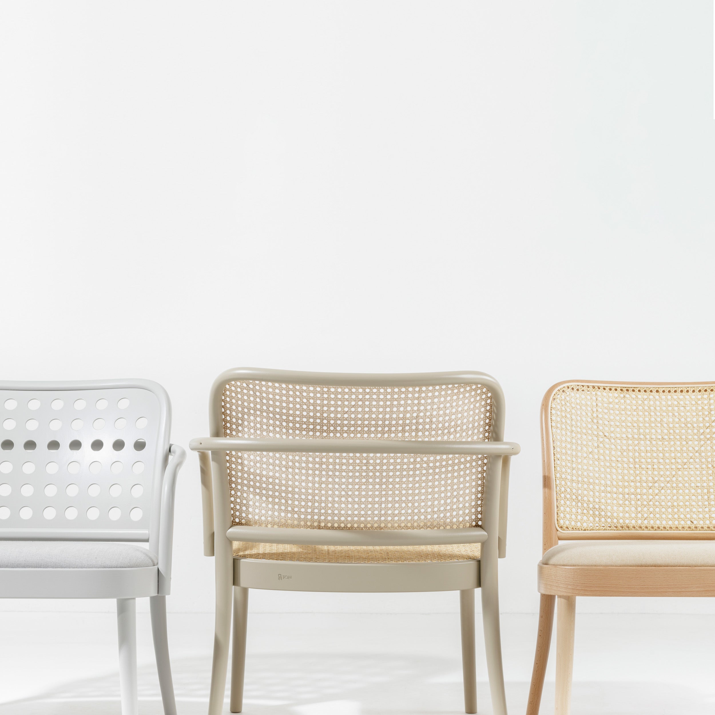 Three Lounge Armchair 822 from TON, embodying Scandinavian minimalism, are side by side against a white background. Inspired by Claesson Koivisto Rune, they showcase perforated backs and seats transitioning from light gray to beige to a natural wood finish.