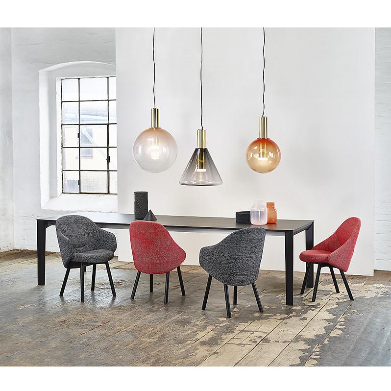 A modern dining room showcases a long black table surrounded by five Armchair Albu chairs from TON in gray and red, offering comfortable upholstery. Overhead, three large pendant lights illuminate the rustic wooden floor, with a grid-patterned window ushering in natural light for added elegance.