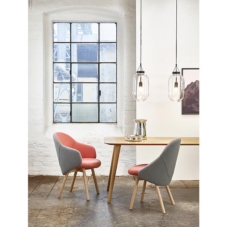 A modern dining area showcases a wooden table with two TON Chair Albu designer chairs in gray and coral, and gray and pink. Glass pendant lights illuminate the white brick wall adorned with a mountain landscape photo, balancing elegance with natural charm.