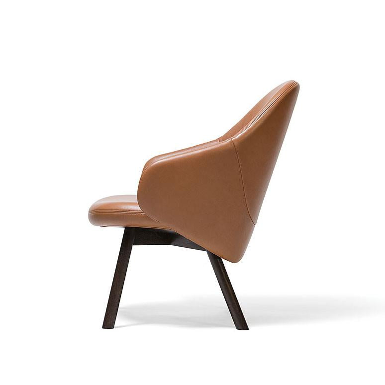 The Lounge Armchair Albu by TON is a modern, brown leather chair with a high backrest, angled armrests, and black wooden legs for perfect ergonomics and a contemporary look.