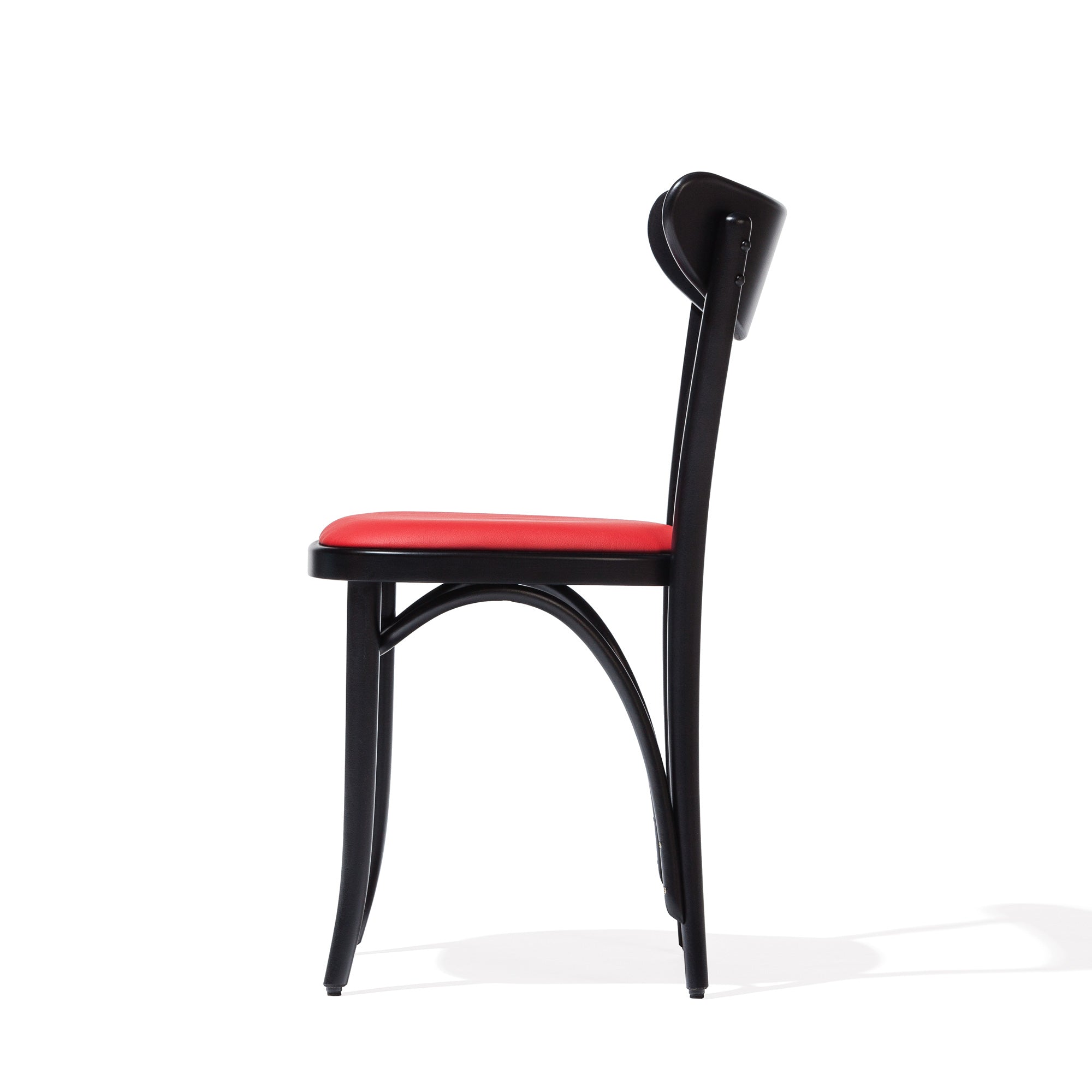 A side view of the TON Chair Banana features a curved plywood backrest and sleek black frame, with a vibrant red upholstered seat creating a striking contrast. The chair casts a faint shadow against a white background.