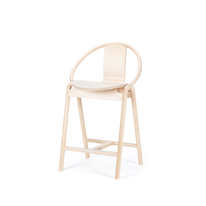 The Barstool Again Upholstered by TON showcases a sleek, modern design with a light wood finish, circular backrest, and clean lines. It features a simple upholstered seat cushion in a neutral color and includes a convenient footrest, making it ideal for any contemporary space.