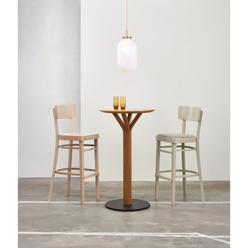 A minimalist dining space features two Barstool Ideal chairs by TON in beige and light gray around a small beechwood table. Two orange glasses sit on the table, while a modern pendant with a frosted glass shade lights the concrete floor.