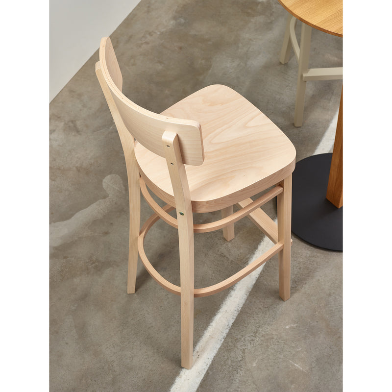A TON Barstool Ideal with a curved backrest and footrest is placed by a round wooden table on a marked concrete floor, merging style and comfort.