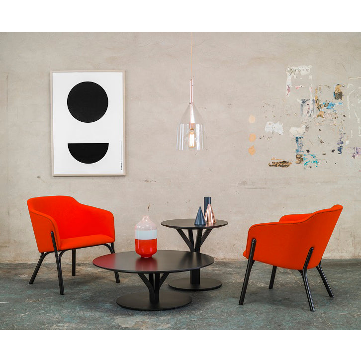 A modern sitting area features two orange chairs, a pair of Bloom Coffee Tables by TON with solid wood tops, and minimalist black-and-white artwork. A pendant light hangs above the concrete wall marked with abstract designs. Vases and decor items adorn the tables.