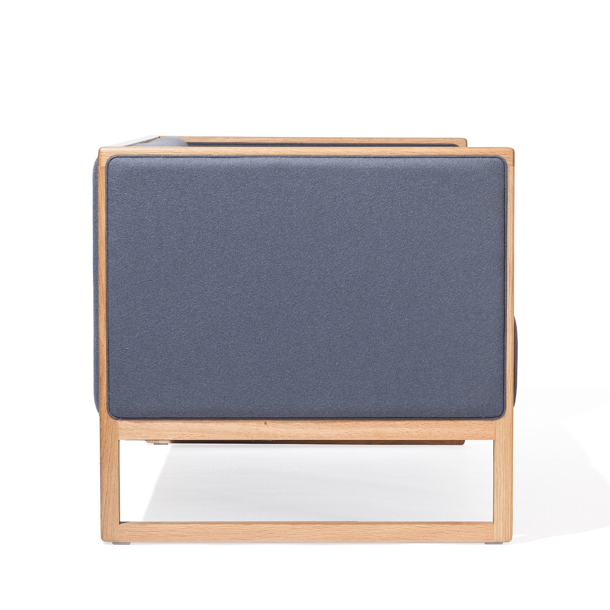 Side view of the Casablanca Sofa by TON, featuring a modern, minimalist design with a dark blue cushioned panel and light wood frame. The clean lines contrast the upholstery against natural wood, enhanced by elegant cane weave armrests.