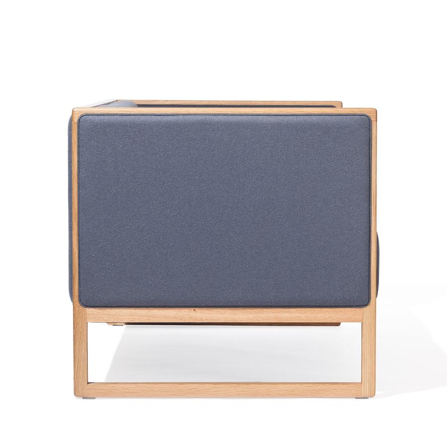 The Armchair Casablanca by TON features a side view of a modern design with a wooden frame, blue upholstered cushioning, open square base, cane weave armrests, and minimalist style for a contemporary look.