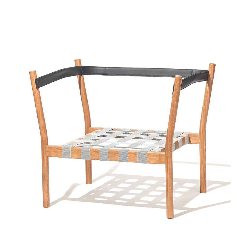 The TON Dowel Lounge Chair features a wooden frame with a black upper backrest and light blue woven seat. This designer armchair has four angled legs, offering a minimalist solitaire-like design that casts graceful shadows on the surface below.