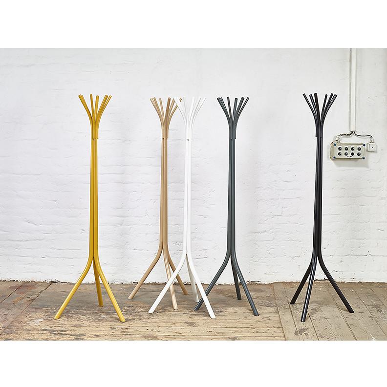 Five Fleur Coat Stands by TON, in yellow, beige, white, gray, and black, line up against a white brick wall. With a sleek minimalist design and beech wood accents at the branches, they perfectly complement the wooden floor and nearby wall socket.