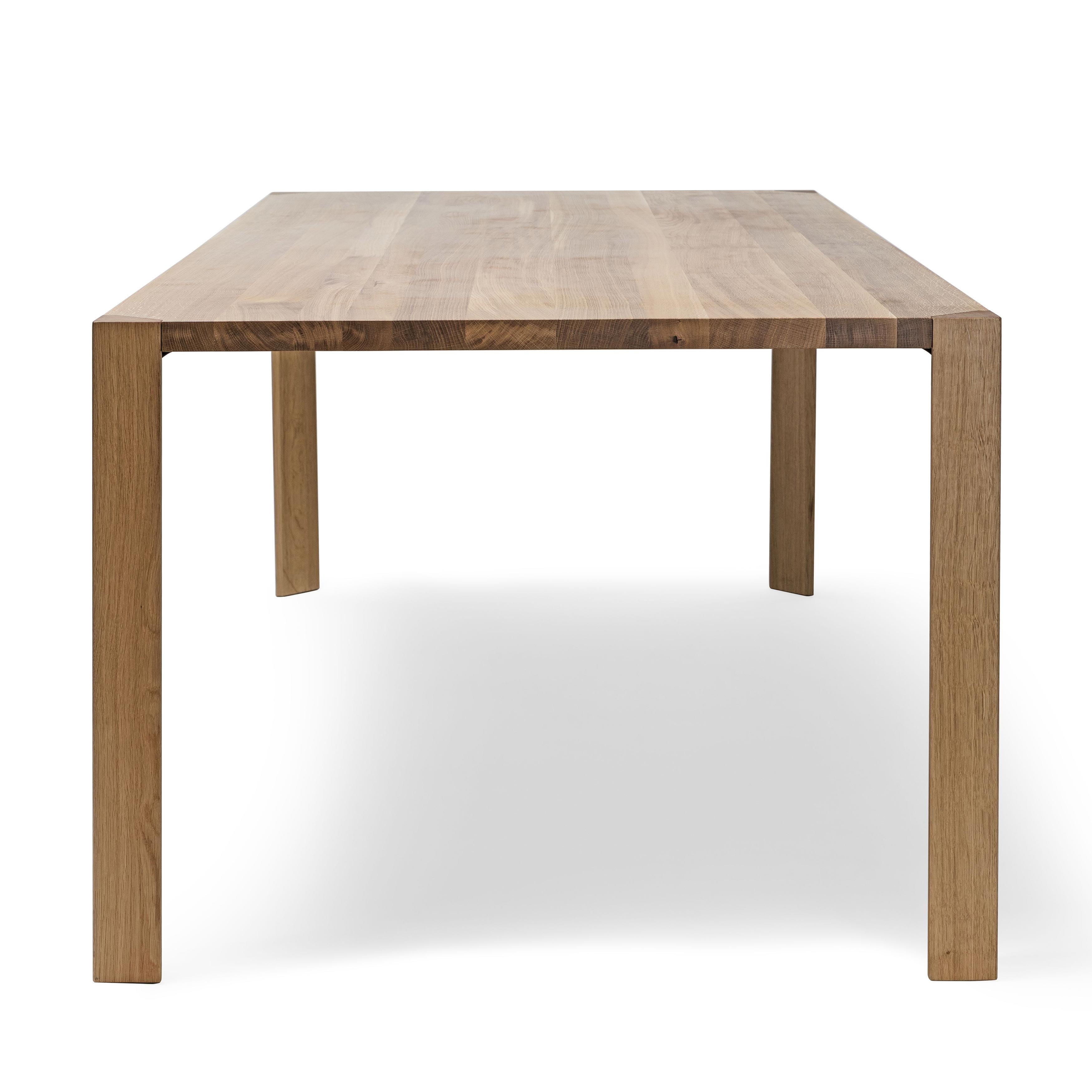 The Table Ink by TON is a minimalist wooden table with a natural grain finish, featuring four sturdy triangular legs and a thin rectangular top set against a plain white background, highlighting its simple and functional design.