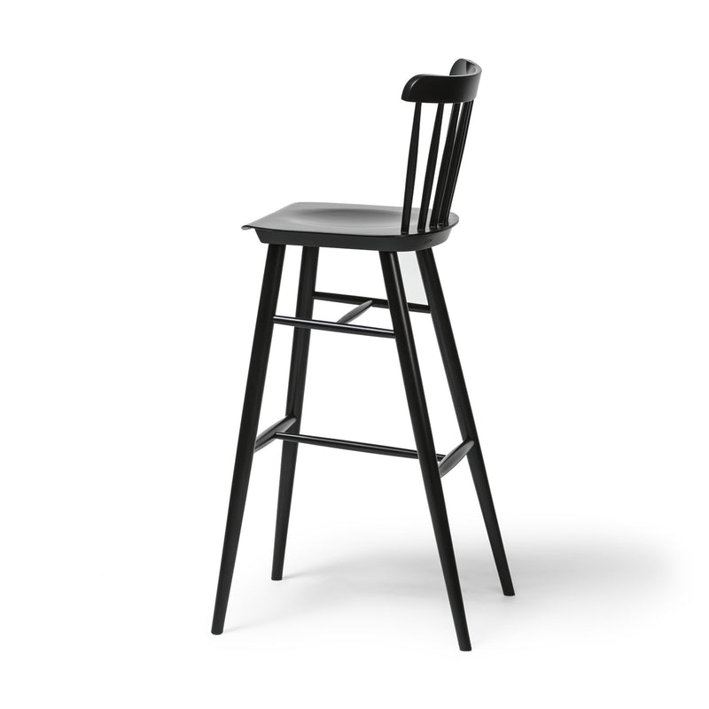 Introducing the Barstool Ironica by TON, crafted from elegant beech and oak. This sleek black wooden stool features a tall backrest, four slightly angled legs with hand-finished dowels, and a footrest connecting the front two legs, all set against a plain white background.