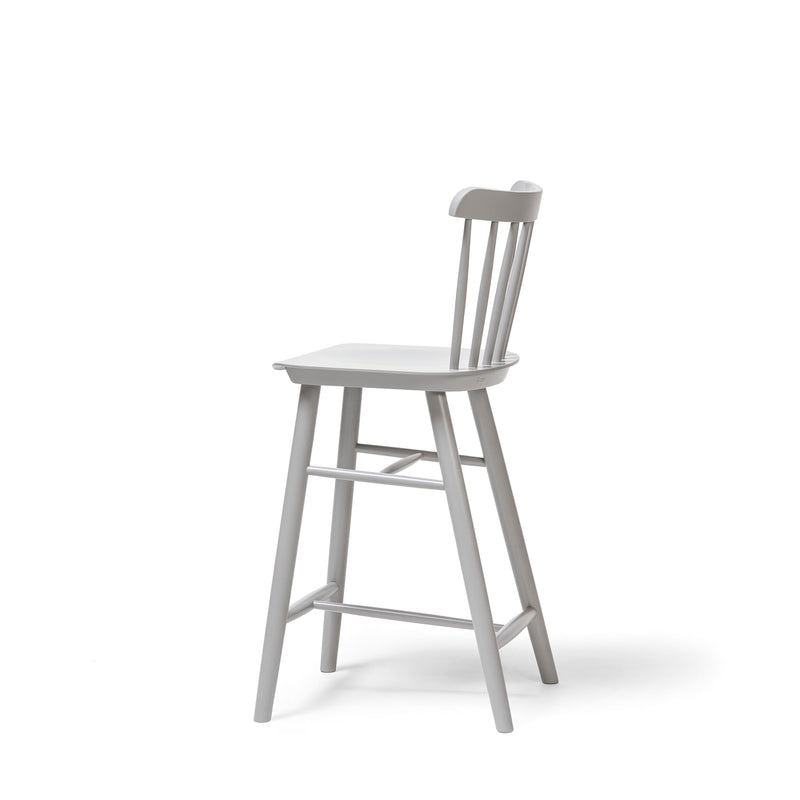 Side view of the TON Counter Stool Ironica, a simple white wooden barstool with a backrest and four beech oak legs. It includes hand-finished dowels and a footrest connecting the front legs, set against a solid white background.