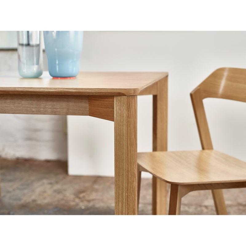 Close-up of the Lasu table by TON, featuring a matching solid wood chair. Two pastel blue vases sit atop the light wooden table. The textured floor and plain wall in the background enhance its minimalist modern look.