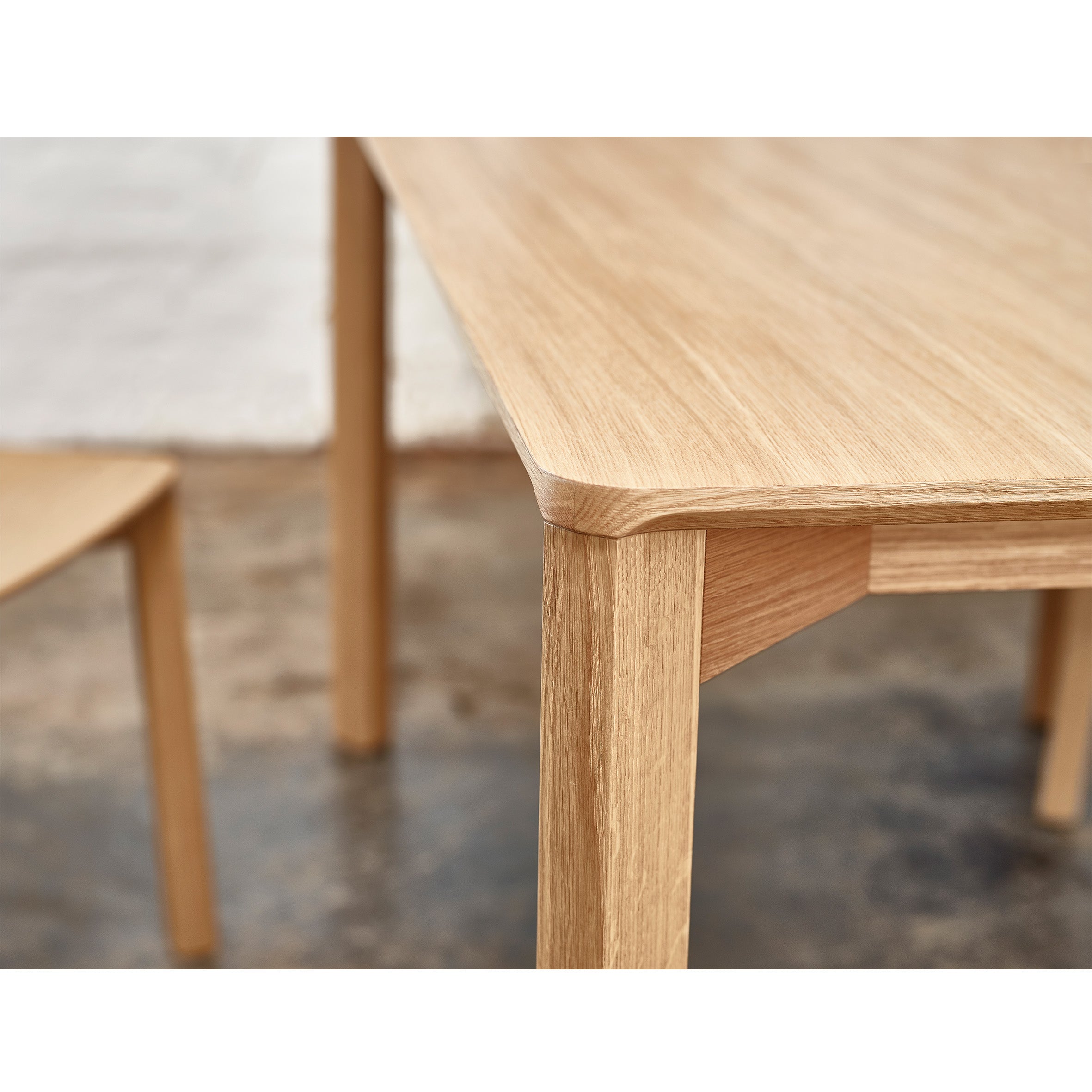 Close-up of the Lasu tables corner by TON, featuring a smooth finish that highlights its craftsmanship. A blurred wooden chair leg can be seen in the background, with a concrete floor contrasting the warm tones to enhance this elegant conference room setting.