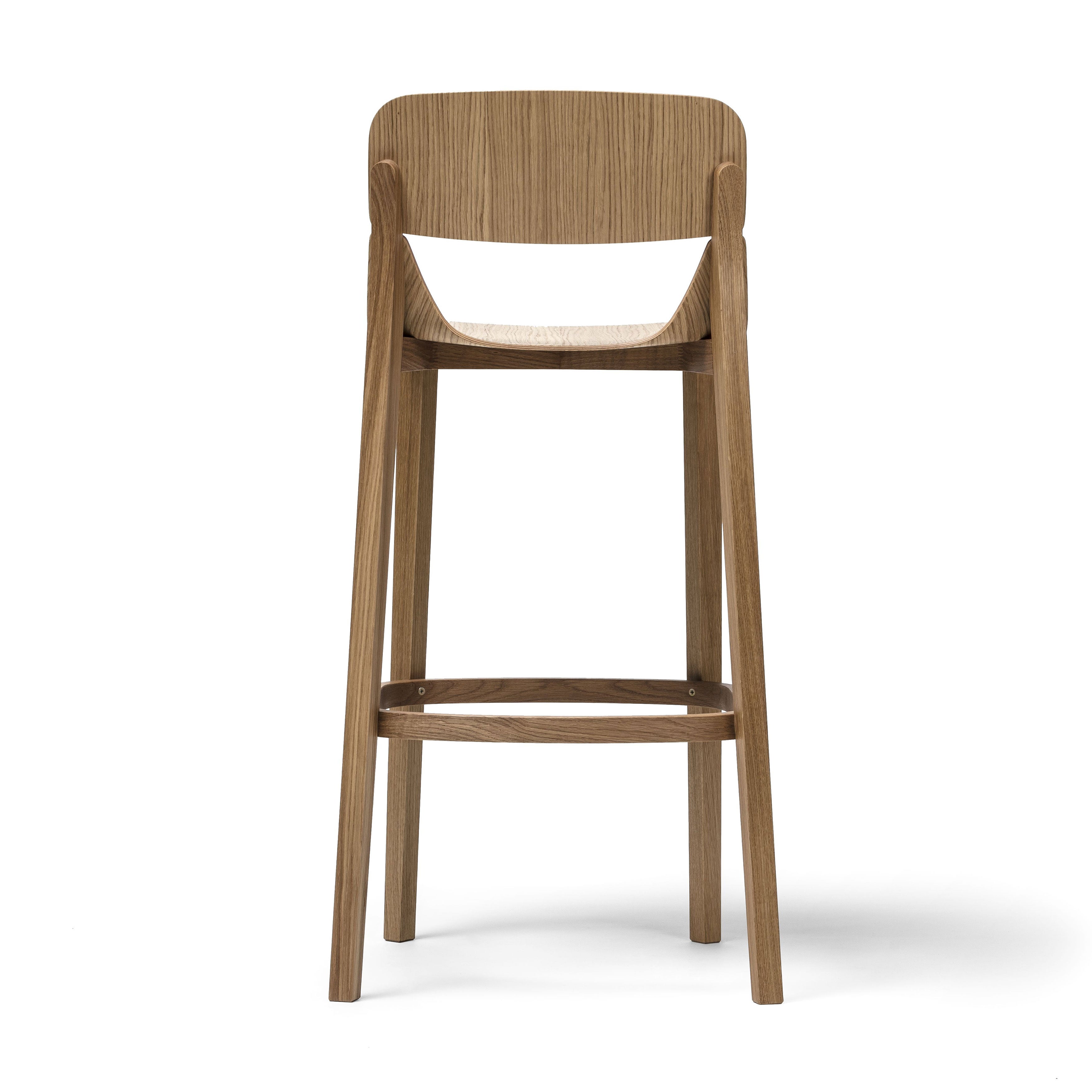 The Barstool Leaf with Backrest by TON features a simple, modern design with ergonomic elements like a curved backrest and contoured seat. It has four sturdy legs connected by a footrest, and the visible wood grain enhances its natural look, making it a standout in any collection.