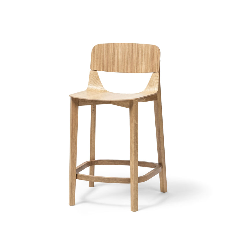 The TON Barstool Leaf with Backrest is a wooden stool featuring a simple, modern design with ergonomic elements like a curved backrest and flat seat. It has four sturdy legs with a footrest, and boasts a light, natural wood finish.