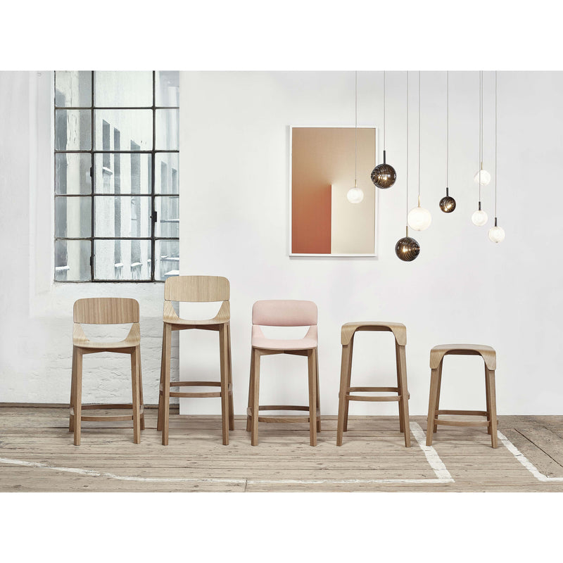In a modern interior, five TON Leaf Barstools with backrests and pastel seats are set against a white wall. Above them is gradient artwork, complemented by spherical pendant lights. Large windows on the left illuminate the scene, enhancing the Leaf collections unique design.