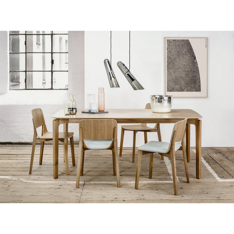 Modern dining room with a wooden table and four TON Chair Leaf dining chairs. Glassware and ceramics adorn the table. Pendant lights hang overhead, with a large window and abstract artwork decorating white walls, while the wooden floor enhances the stylish ambiance.