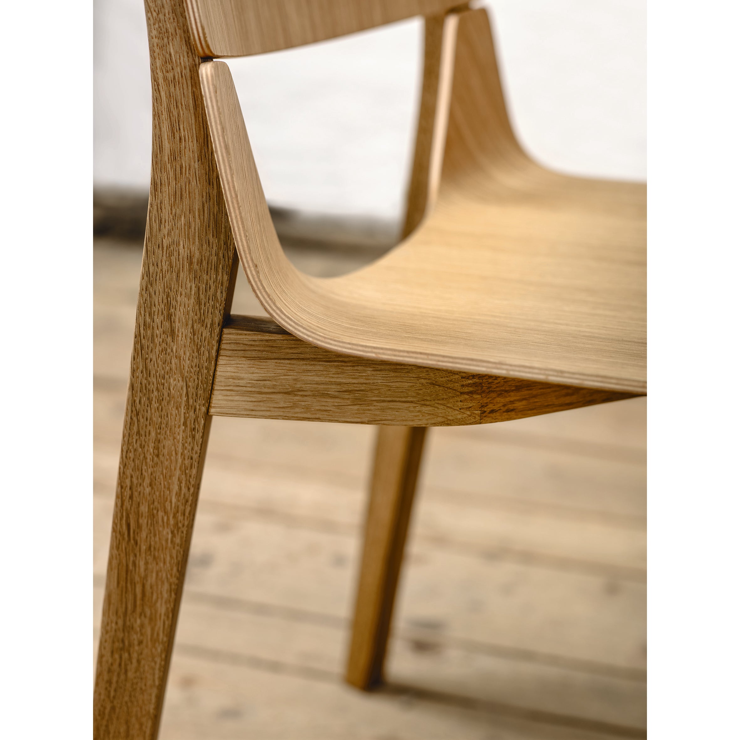 The Chair Leaf - Upholstered by TON features a sleek, minimalist design with smooth, curved lines for ergonomic comfort. Its visible wood grain stands out against a light wood floor and off-white wall.