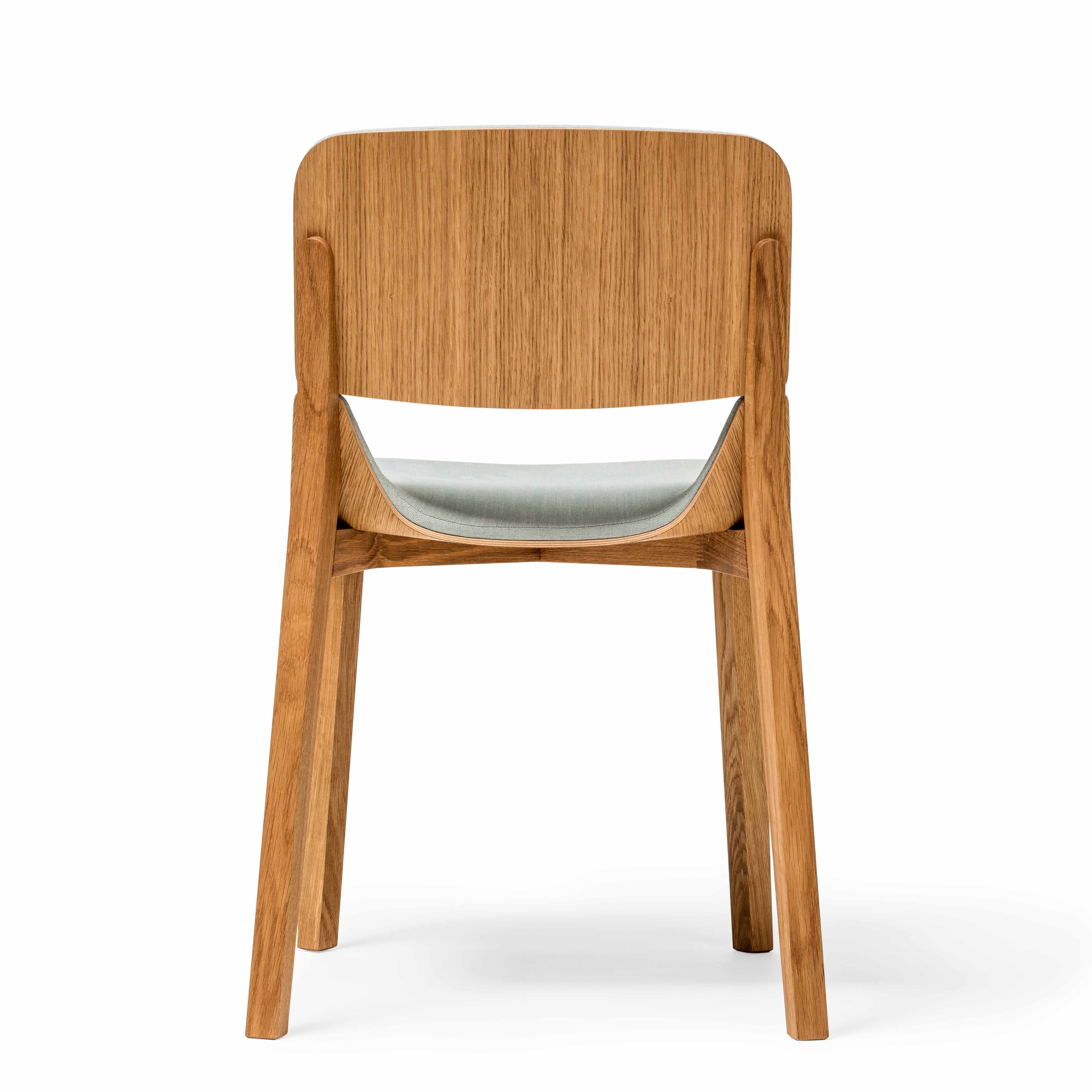 The Chair Leaf - Upholstered by TON is a wooden dining chair featuring a curved backrest, light gray cushioned seat, and slightly angled legs for ergonomic appeal and minimalist design, all set against a plain white background.