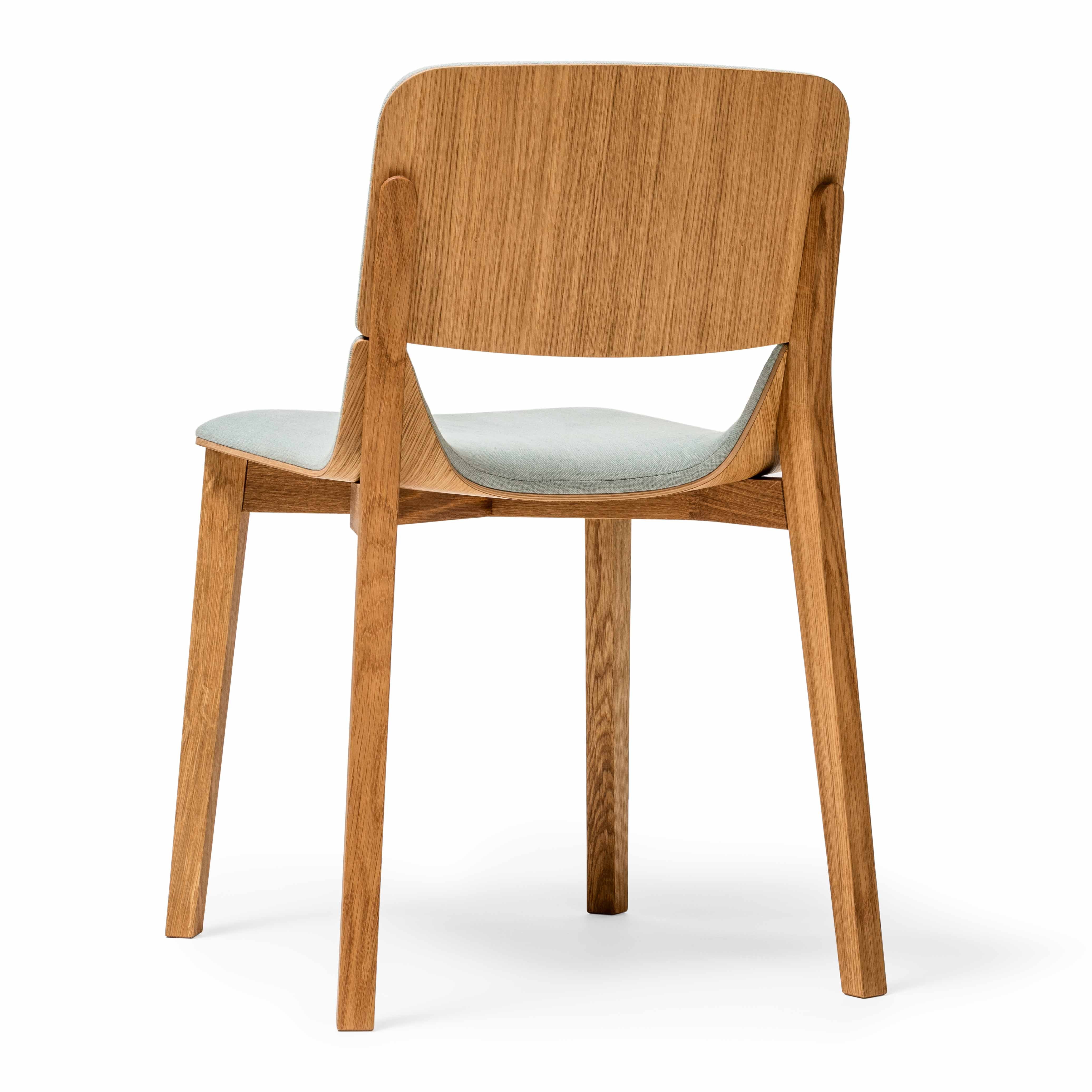 The Chair Leaf - Upholstered by TON is a wooden dining chair with light upholstery. Its ergonomic design features a sleek, minimalistic look with a curved backrest and four straight legs.