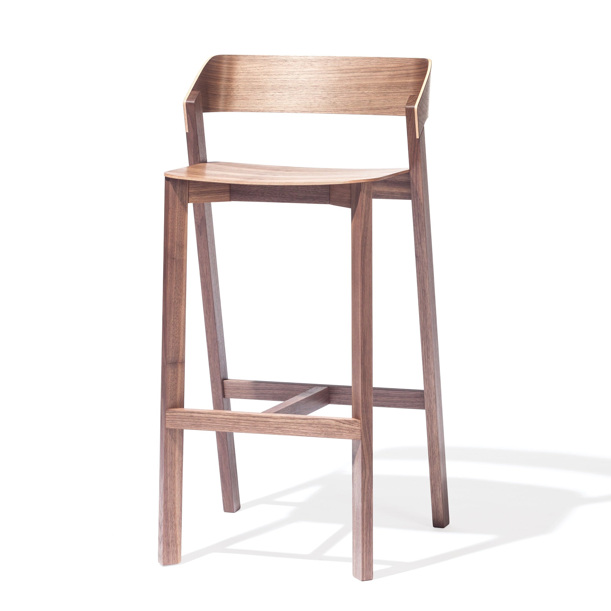 TONs Barstool Merano features a minimalist design with a curved backrest, four straight legs, and a slightly angled seat for enhanced comfort. Crafted from solid wood with a natural finish, it beautifully highlights the wood grain and includes a footrest connecting the front legs.