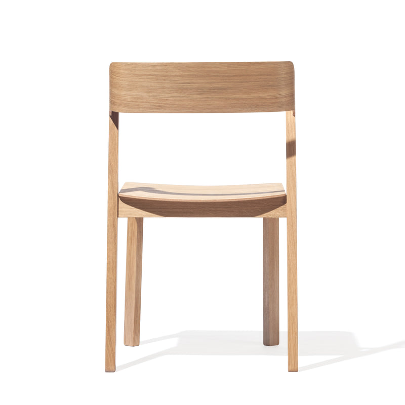 The Chair Merano by TON showcases a sleek, modern design made from solid wood, with a flat seat and subtly curved backrest against a plain white background highlighting its natural wood grain.