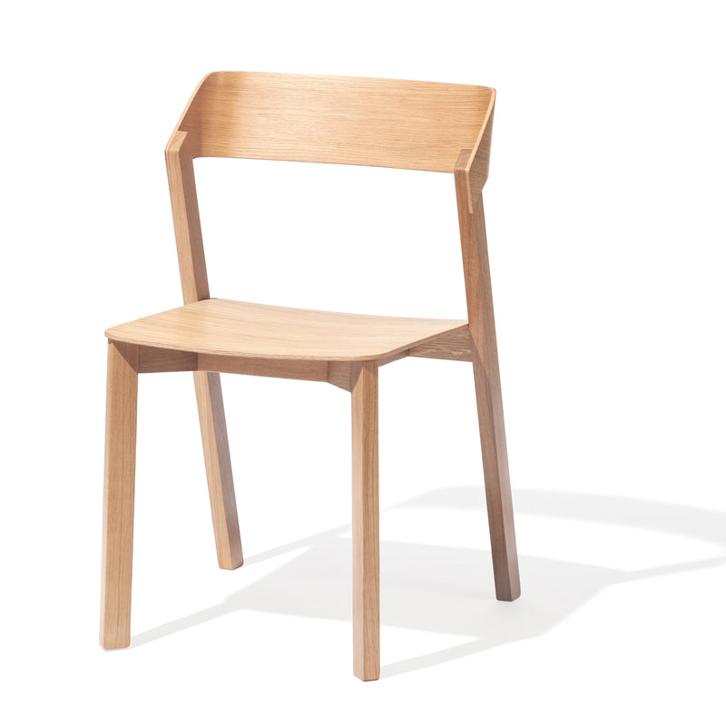 The Chair Merano by TON is a modern, minimalist dining chair crafted from bent plywood with a light brown finish. It features a straight backrest and four simple legs, casting shadows on a pristine white background.