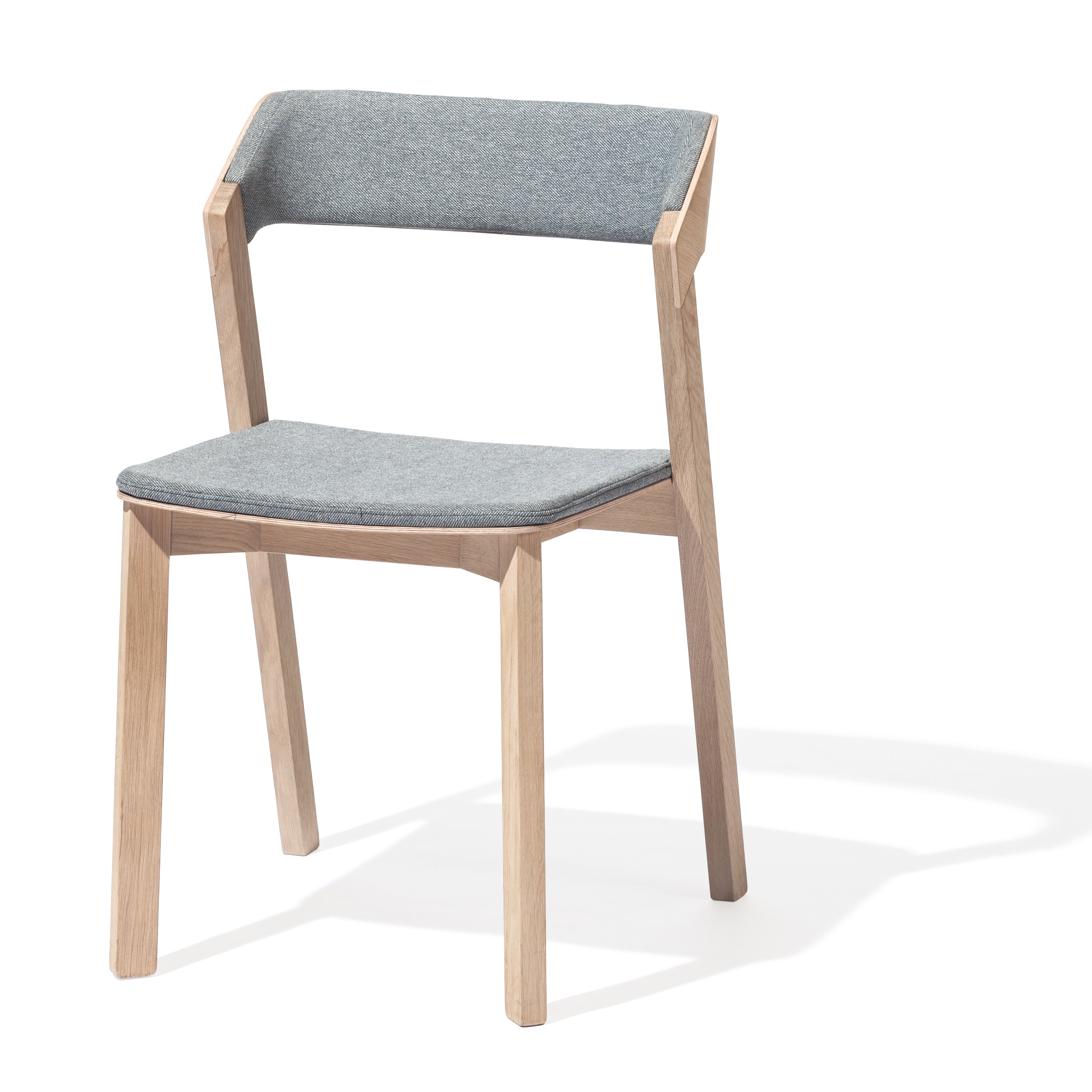 The Chair Merano - Upholstered by TON features a light wood frame and grey upholstered seat and backrest, showcasing a minimalistic, contemporary design with clean lines and angled solid wood legs. It casts a subtle shadow on a white background.