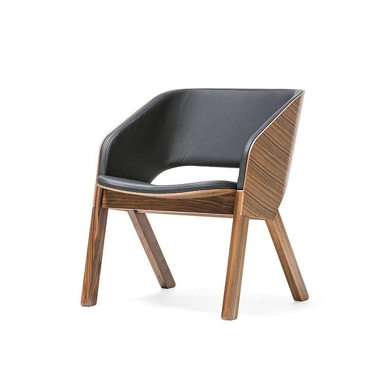 The Merano Lounge Armchair by TON features a sleek, contemporary design with solid wood legs and a curved frame. The cushioned seat and backrest are crafted from bent plywood and covered in black leather or similar material.